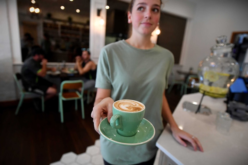 Waitress looking to the side while holding a cup of coffee balanced on a saucer